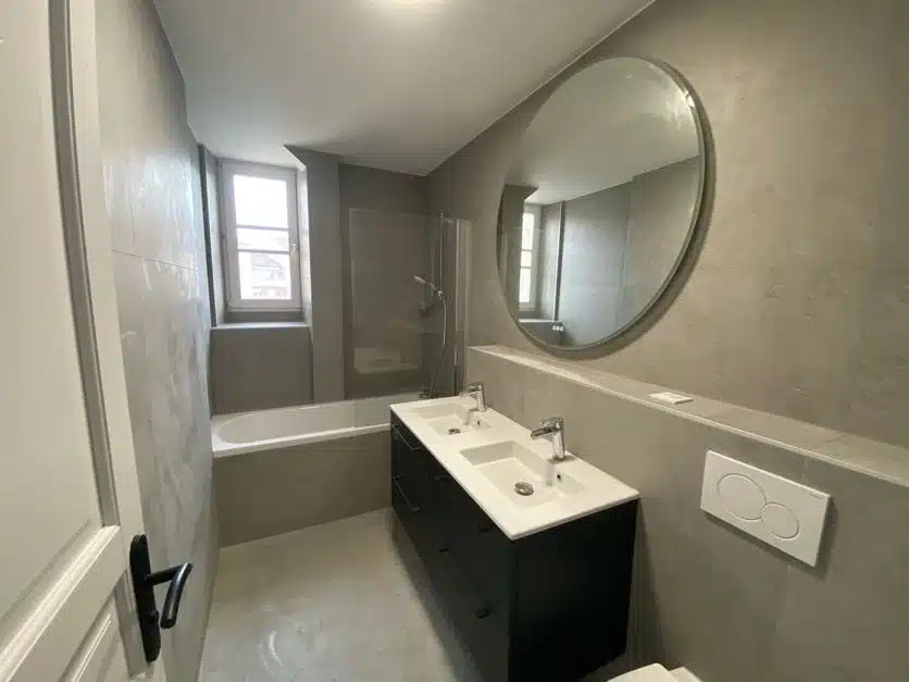Salle de bains contemporaine rénovée à Annemasse avec grand miroir rond et double vasque.