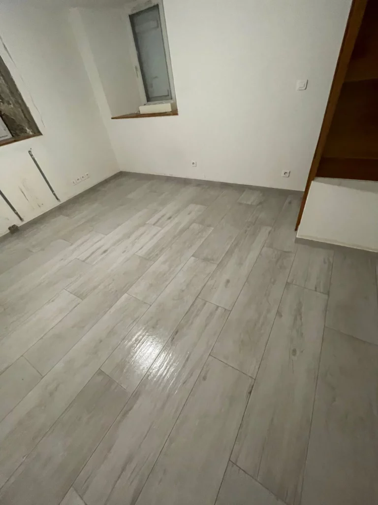 Pose d'un carrelage imitation parquet lors d'une rénovation carrelage à Bons-en-Chablais dans une pièce vide.