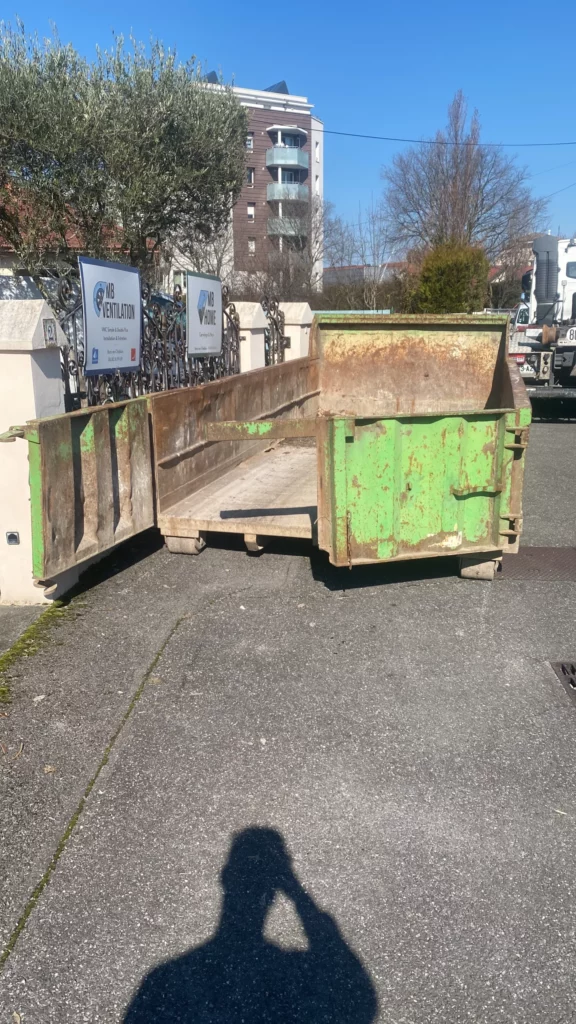 Benne à gravats verte stationnée devant le chantier de démolition d'une grande maison à Annemasse.
