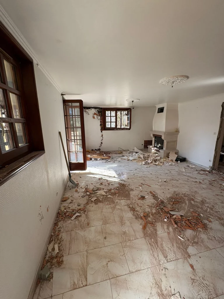 Sol dégagé après la démolition partielle d'une grande maison à Annemasse avec une pelle au mur.