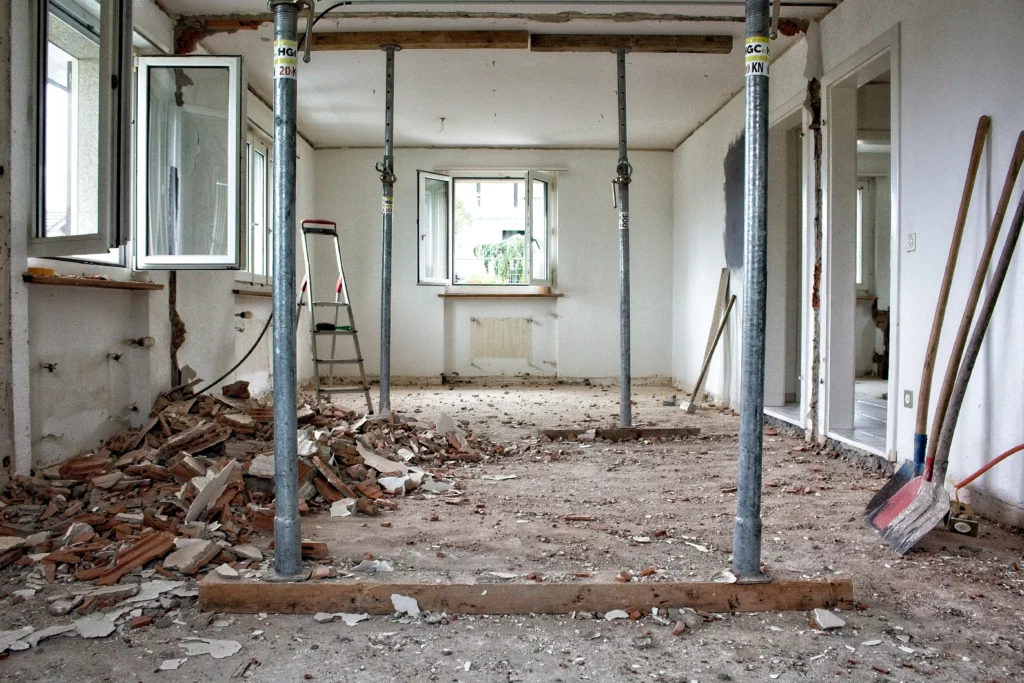 Intérieur d'un bâtiment en démolition MB-Home avec gravats de briques, étais métalliques de soutien et pelles.