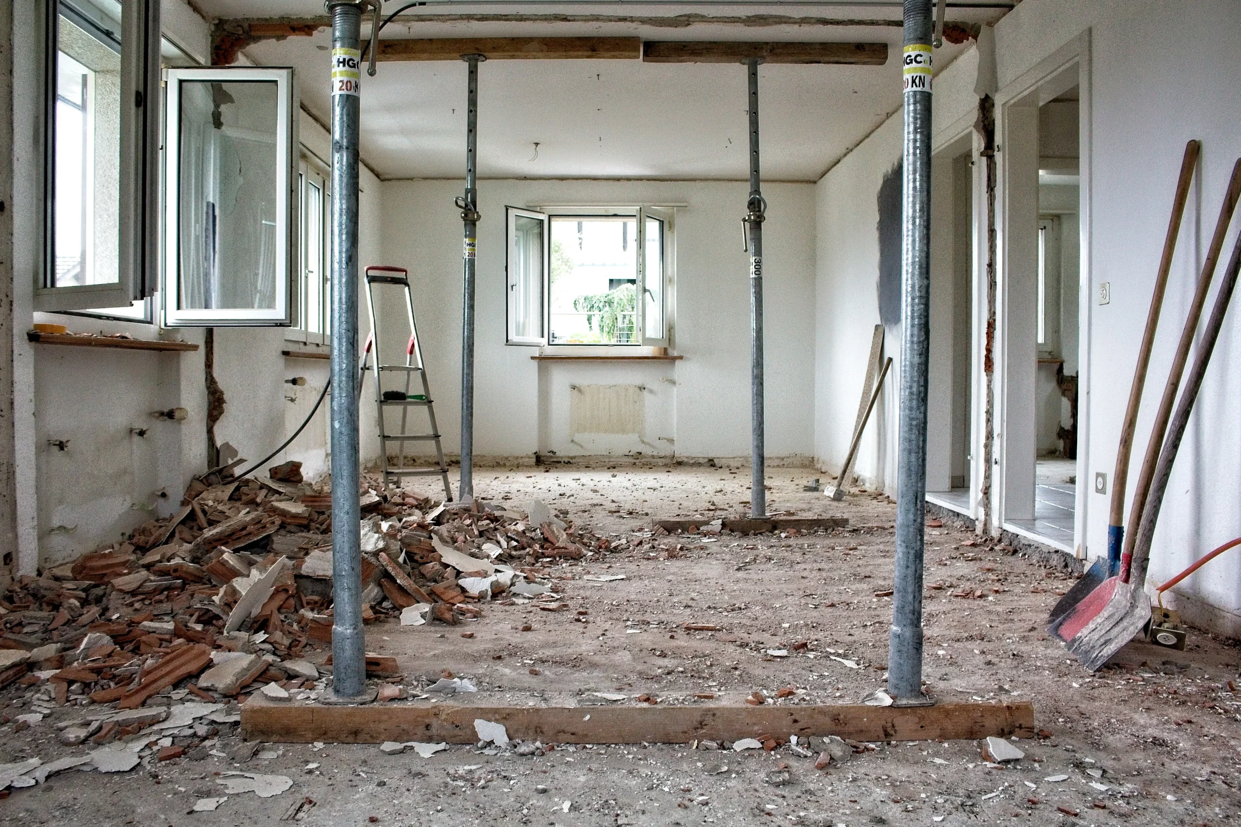 Intérieur d'un bâtiment en démolition MB-Home avec gravats de briques, étais métalliques de soutien et pelles.