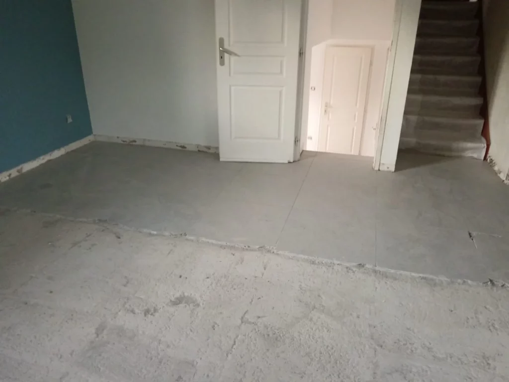 Démolition du carrelage d'une maison à Excenevex : pièce avec sol nu et quelques carreaux restants avant travaux