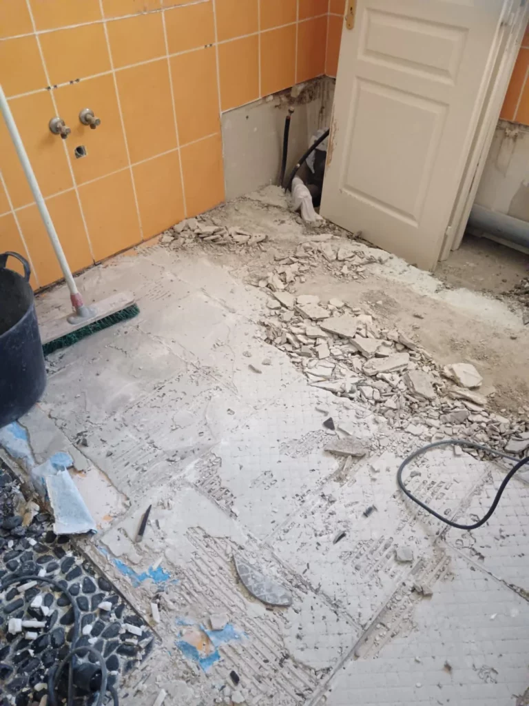 Démolition du carrelage d'une salle de bain à Excenevex : sol arraché avec gravats et faïence orange au mur