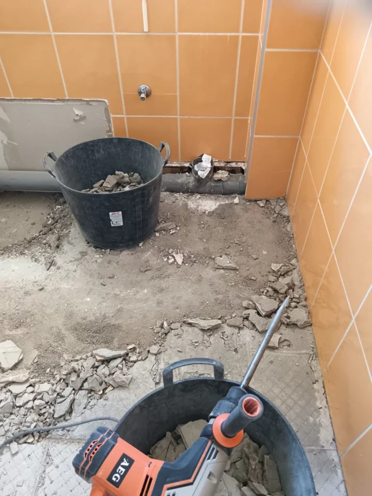 Démolition du carrelage salle de bain à Excenevex : seau plein de gravats et burineur AEG, faïence orange visible
