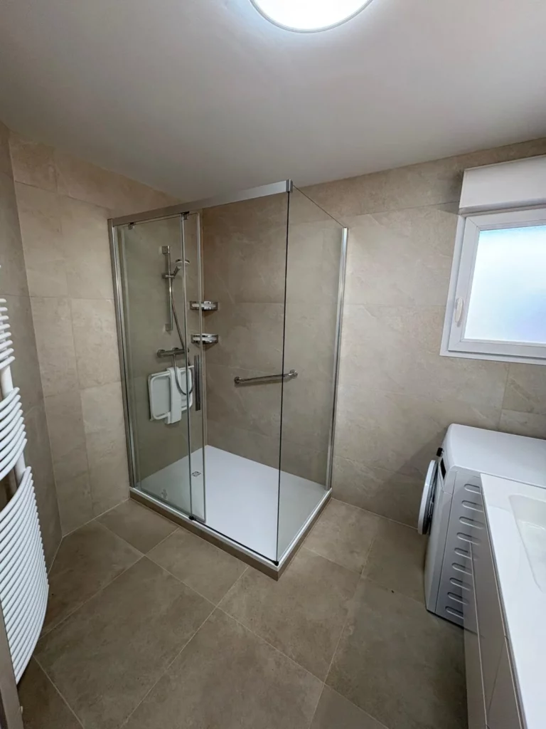 Cabine de douche avec carrelage rénové à Annemasse, paroi en verre, receveur blanc et barre d'appui chromée