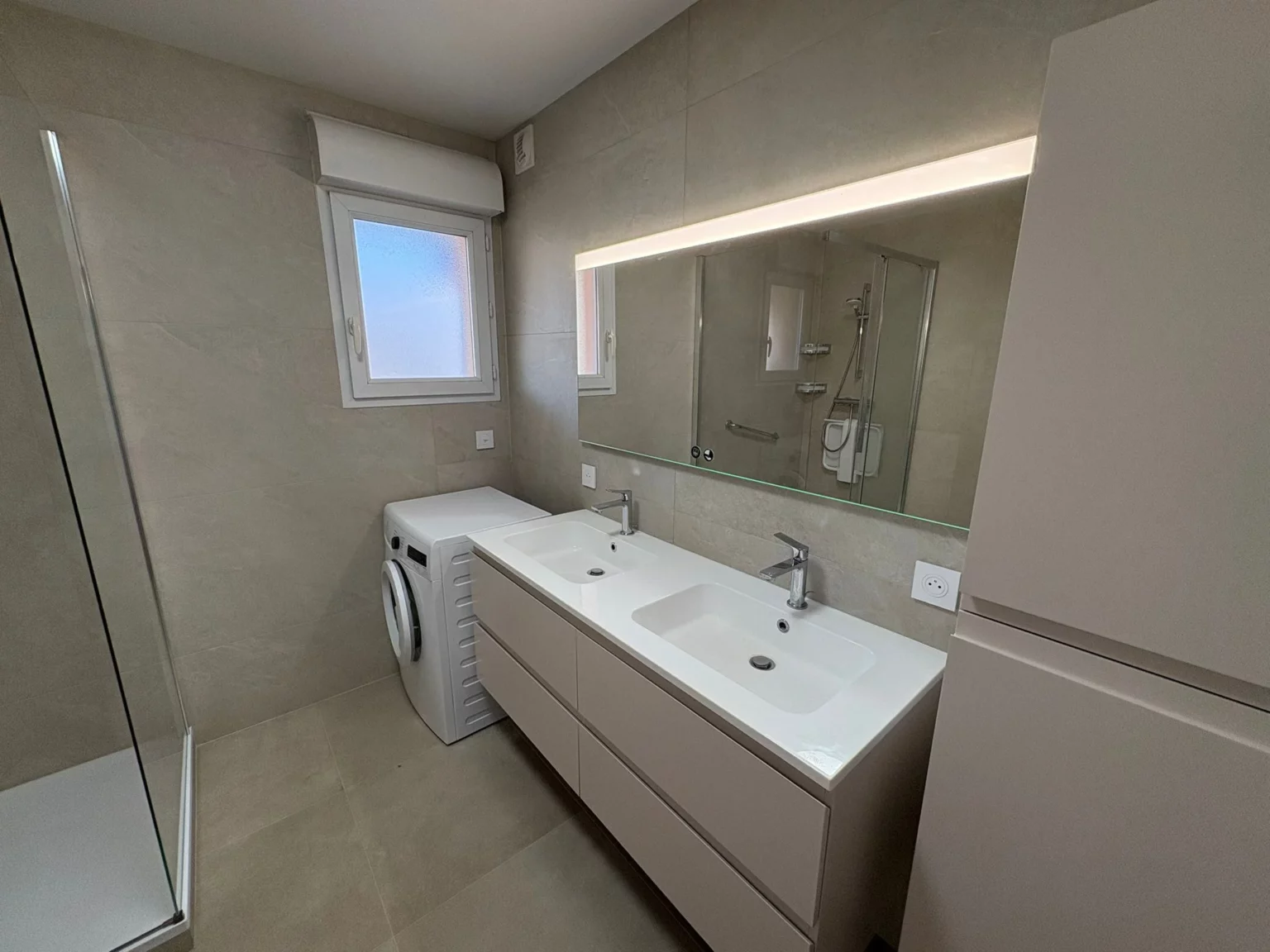 Salle de bain rénovée à Annemasse avec double vasque, meuble suspendu beige et grand miroir rétroéclairé