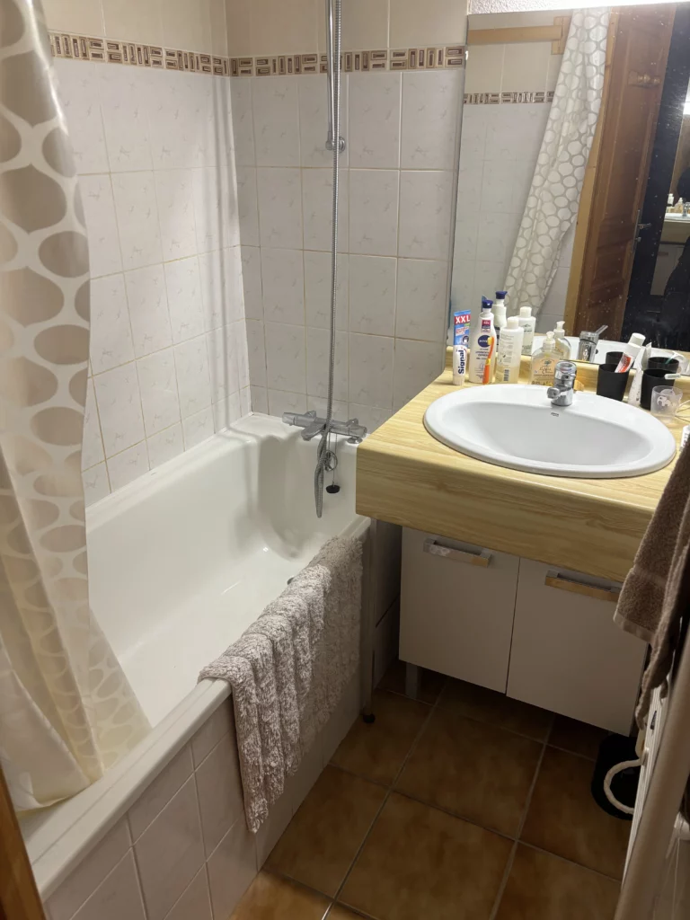 Salle de bain avant rénovation à Châtel avec baignoire, rideau de douche et vasque bois