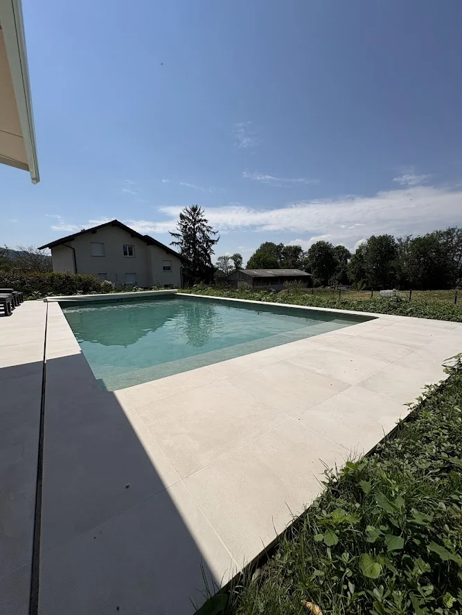 Terrasse en carrelage clair terminée à Brenthonne bordant une piscine à débordement