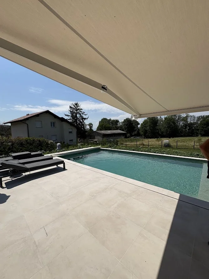 Terrasse en carrelage à Brenthonne équipée d'un store banne surplombant la piscine