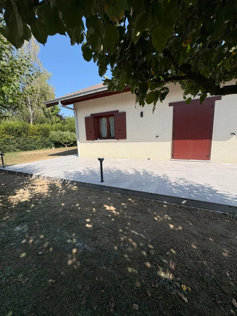 Terrasse en carrelage gris devant une maison aux volets rouges à Bons-en-Chablais après rénovation
