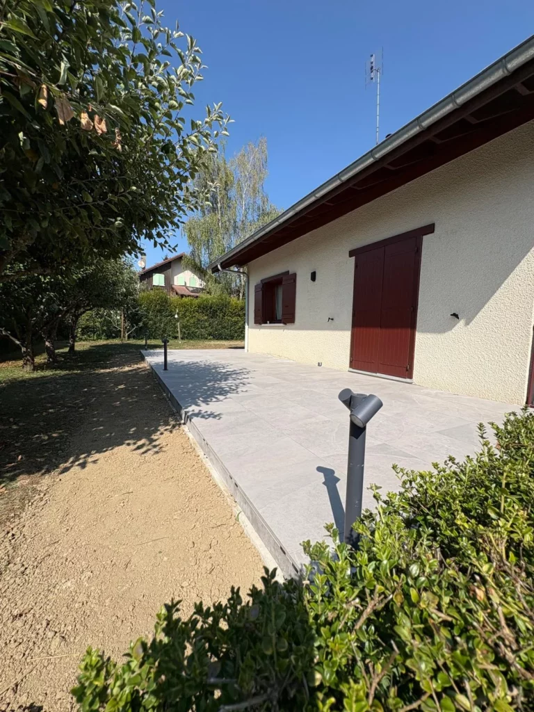 Vue latérale d'une terrasse en carrelage gris rénovée à Bons-en-Chablais bordée de bornes lumineuses