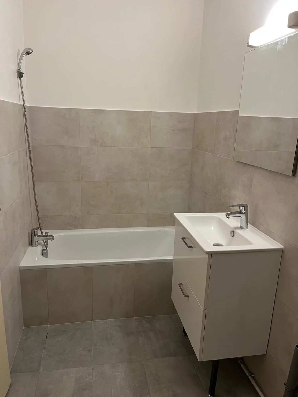 Rénovation d'une salle de bain à Douvaine : baignoire, meuble vasque blanc à tiroirs, miroir et carrelage beige neuf
