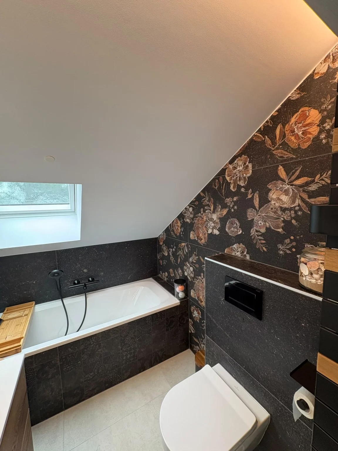 Rénovation d'une salle de bain à Fessy : baignoire noire et carrelage fleuri après travaux, vue rapprochée