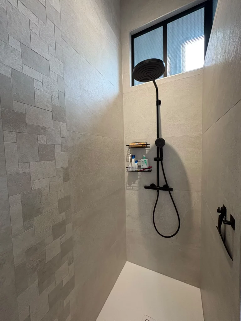 Rénovation d'une salle de bain à Fessy : douche à l'italienne après travaux avec carrelage gris et colonne noire