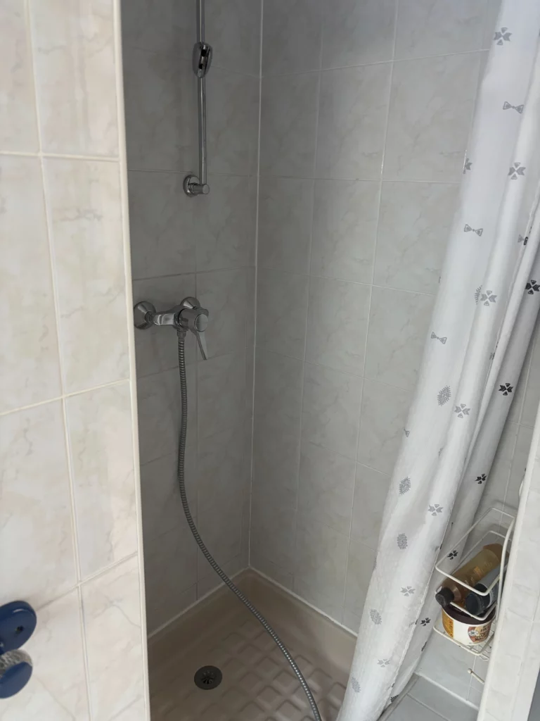 Rénovation d'une salle de bain à Fessy : douche avant travaux avec rideau et carrelage blanc effet marbre